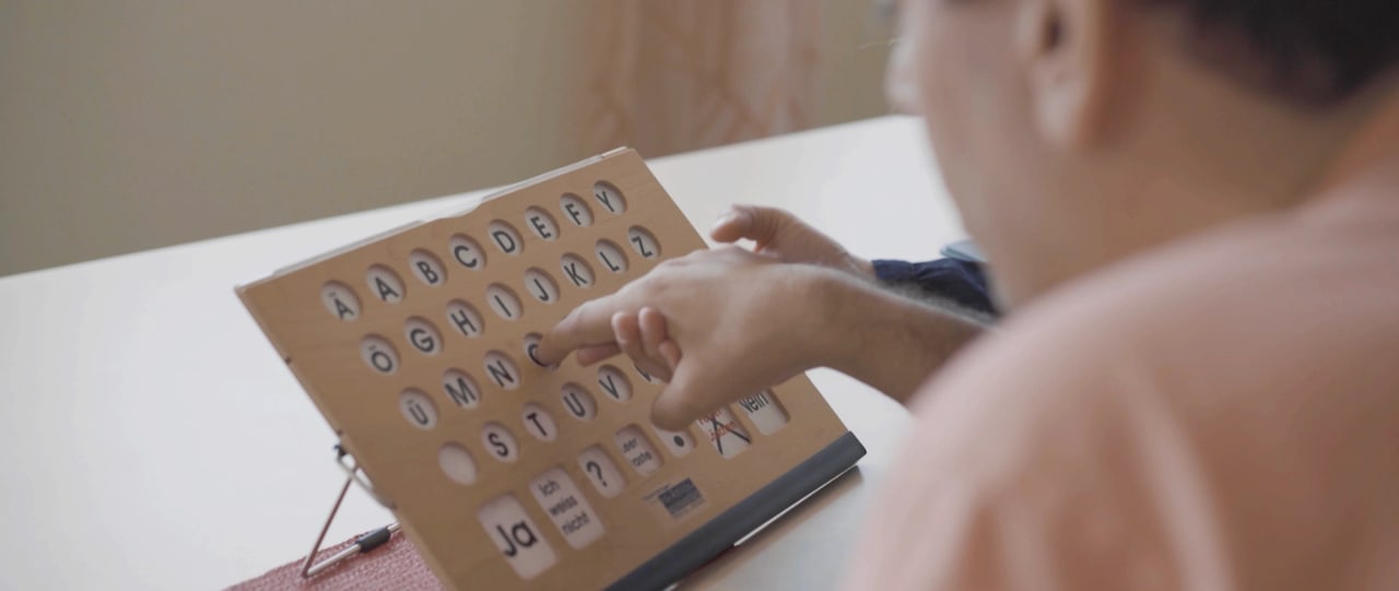 Eine Hand zeigt auf Buchstaben einer Kommunikationstafel