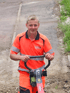 Junger Mann in oranger Arbeitskleidung bedient eine Rüttelplatte auf Baustelle.