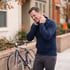 A man in a blue jacket winces while holding his neck outdoors next to a bicycle.