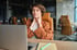 A woman holding her painful neck while working on a laptop.