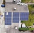 Dach eines Hauses mit drei Gruppen von Solarmodulen, einer dunklen Limousine und einer Grünfläche.
