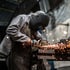 Schweißer in Schutzkleidung arbeitet mit einer Schleifmaschine und erzeugt Funken.