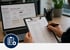 Hände füllen ein Klemmbrett für Aufgabenmanagement vor einem Laptop mit geöffnetem Web-Portal aus - Software für Alarmierung - Notfall- und Krisenmanager (NKM®).