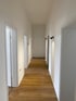 Weißer Korridor mit Holzboden, mehreren Türen und modernen schwarzen Wandleuchten an beiden Seiten.