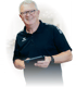 Lächelnder Mann mit Brille im schwarzen Erima-Poloshirt hält ein Tablet in den Händen.