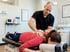 Male chiropractor performing a spinal adjustment on a woman lying face down on a chiropractic table in a clinic.