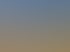 Frau trainiert braunes Pferd auf sandigem Reitplatz mit grüner Umzäunung bei Sonnenuntergang.