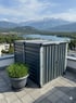 Zwei graue Gartenboxen auf einer Dachterrasse mit Alpen- und Seeblick, daneben ein Topf mit Gras.