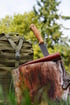 Ein Messer mit Holzgriff und brauner Lederscheide steckt in einem Baumstumpf neben einem grünen Rucksack.
