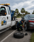 Towing Port Charlotte roadside assistance technician changing a flat tire on a sedan beside a tow truck.