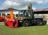 Grüner Unimog mit orange-roter Schneefräse vor einer Halle auf Grasfläche stehend.