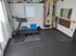 Heim-Fitnessraum mit Laufband, Sprossenwand und Trainingsmatten auf dunklem Boden.