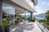 Moderne Terrasse mit großen Glasschiebetüren, Blick auf einen See und Berge unter blauem Himmel.