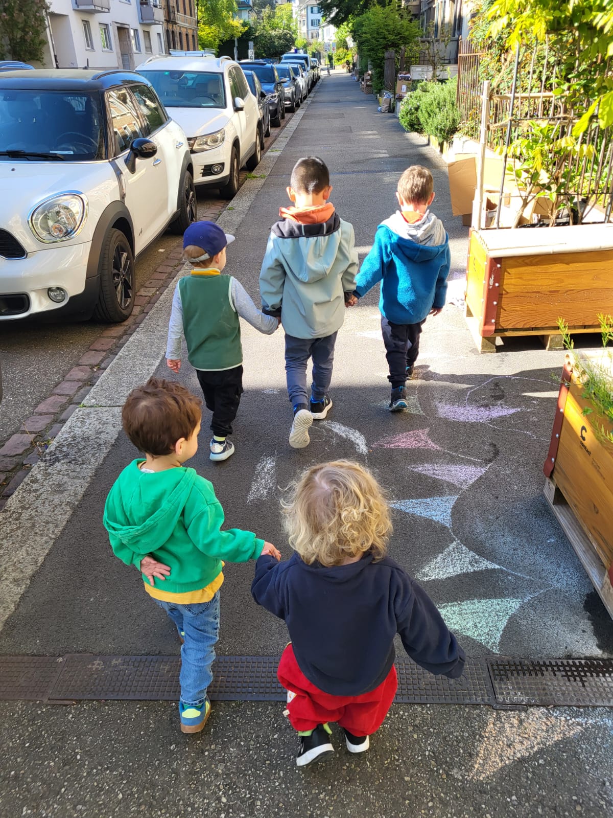 Kinder gehen Hand in Hand über die Strasse, von hinten fotografiert.