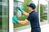 Ein Fensterputzer in blauer Uniform und Handschuhen reinigt ein Fenster mit einem Abzieher und einem Tuch.