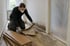 Handwerker mit Schutzbrille und Maske entfernt durchnässtes Laminat und Trittschalldämmung, die Wand zeigt einen Feuchterand