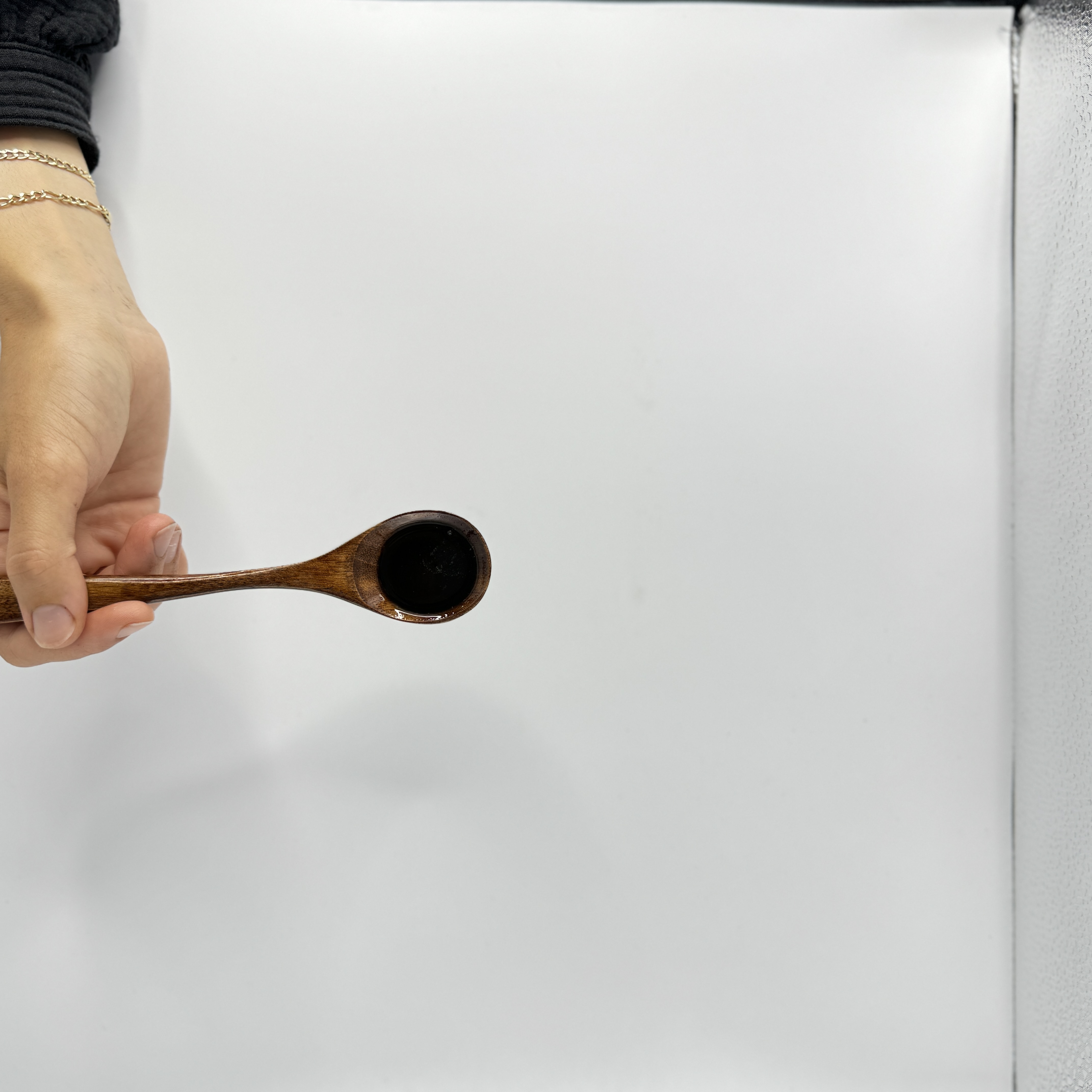 Frauenhand hält Holzlöffel mit fast schwarzem ungefilterten Schwarzkümmelöl