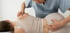 Chiropractor adjusts a woman's back and shoulder while she lies sideways.
