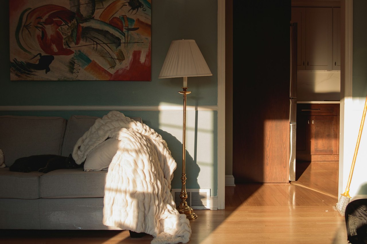Ein ruhiges Wohnzimmer am Nachmittag, Sonnenlicht fällt auf ein Sofa mit Wolldecke und eine Stehlampe