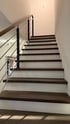 Eine moderne Treppe mit dunkelbraunen Holzstufen, weißen Setzstufen und einem Geländer aus Holz, Schwarzmetall und dünnen Metallstäben.
