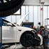Zwei Mechaniker reparieren einen weißen Tesla auf einer Hebebühne in einer Werkstatt.
