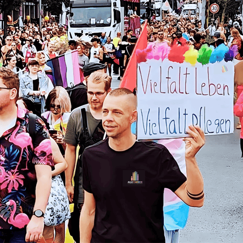 Person hält ein Schild mit der Aufschrift Vielfalt leben, Vielfalt pflegen bei einer Pride-Parade