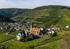 Dorf Beilstein an der Mosel mit Kirche und Burgruine, umgeben von Weinbergen im Herbst.