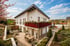 Modernes weißes Haus mit Balkon, Terrasse, Garten und Außenmöbeln unter blauem Himmel.