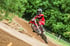 Motocrossfahrer in roter Ausrüstung springt mit Motorrad über einen Erdhügel.