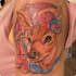 Farbiges Tattoo auf einem Oberarm, das ein Rehkitz mit Blumenkranz und umrahmenden Blütenumrissen zeigt.