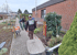 Gärtner bei Gartenarbeiten mit Schubkarre und Schaufeln vor einem Backsteingebäude.