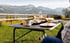 Ein gedeckter Campingtisch mit Essen und Getränken vor einer Berglandschaft.