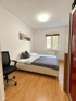 Helles Schlafzimmer mit Doppelbett, Laminatboden, schwarzem Bürostuhl, Wandbild und Fenster mit Blick ins Grüne.