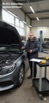 Ihr Kfz-Gutachter - Stephan Nienhues. Mann mit Tablet und Stift prüft Motorraum eines grauen Mercedes der einen Schaden hatte.