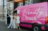 Drei Frauen stehen lächelnd neben einem pinken Mercedes-Benz Beauty Truck mit offener Tür.