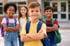 Vier lächelnde Kinder mit Rucksäcken stehen vor einem Schulgebäude, die Arme verschränkt.