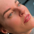 Eine Frau mit Permanent-Make-up an Augenbrauen und Lippen blickt nach oben und lächelt leicht.