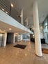 Geräumige, moderne Lobby mit Fliesenboden, Aufzügen, Rezeption und einer oberen Galerie mit Geländer.