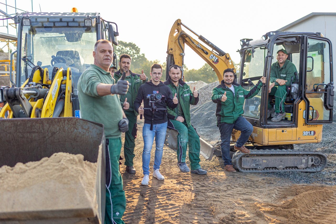 Sechs Mitarbeiter eines Kundenbetriebs stehen vor Baggern auf einer Baustelle