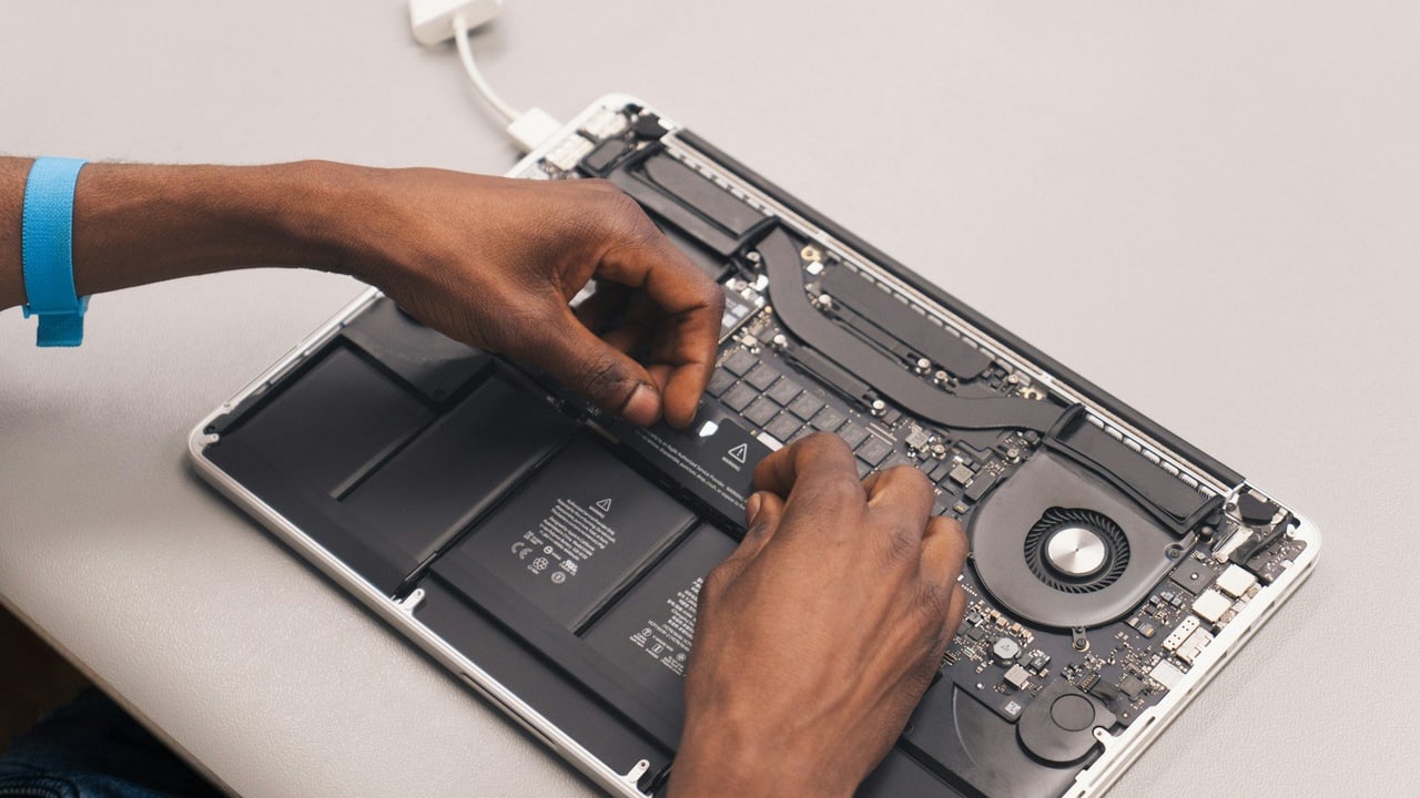 Hände arbeiten an einem geöffneten MacBook, Akku und Lüfter sind sichtbar