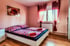 Schlafzimmer mit Doppelbett, rosa Wänden, Holzfußboden und einem Fenster mit roten Vorhängen.