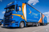 Blauer Scania-LKW mit orangefarbenen Akzenten und "protonx professional logistics"-Logo auf der Seite.