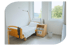 Leeres Krankenhauszimmer mit Holzrahmenbett, Nachttisch und zwei großen Fenstern.