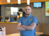 Ein McDonald's-Mitarbeiter in blauem Hemd mit gekreuzten Armen lächelt in einem Restaurant.