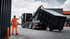 Ein Abrollkipper-LKW setzt einen großen schwarzen Container ab, während ein Arbeiter in Warnkleidung Einweisungen gibt.