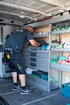 Mitarbeiter in Arbeitskleidung sortiert Werkzeug in einem professionell mit Regalsystemen ausgebauten Transporter.