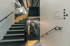 Eine Treppe mit grauen Stufen und gelben Akzenten, daneben eine weiße Wand mit Wegweisern und Piktogrammen.