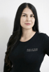 Eine Frau mit langen schwarzen Haaren und schwarzem Oberteil mit dem Logo "DELUXE LASER & BEAUTY".