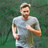 Man in a gray t-shirt running outdoors with blurred green trees in the background.