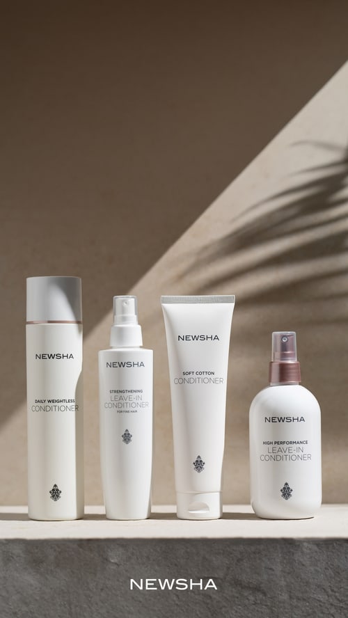 Vier weiße Newsha Haarpflegeprodukte, darunter Leave-In Conditioner und Soft Cotton Conditioner, vor Palmenschatten.